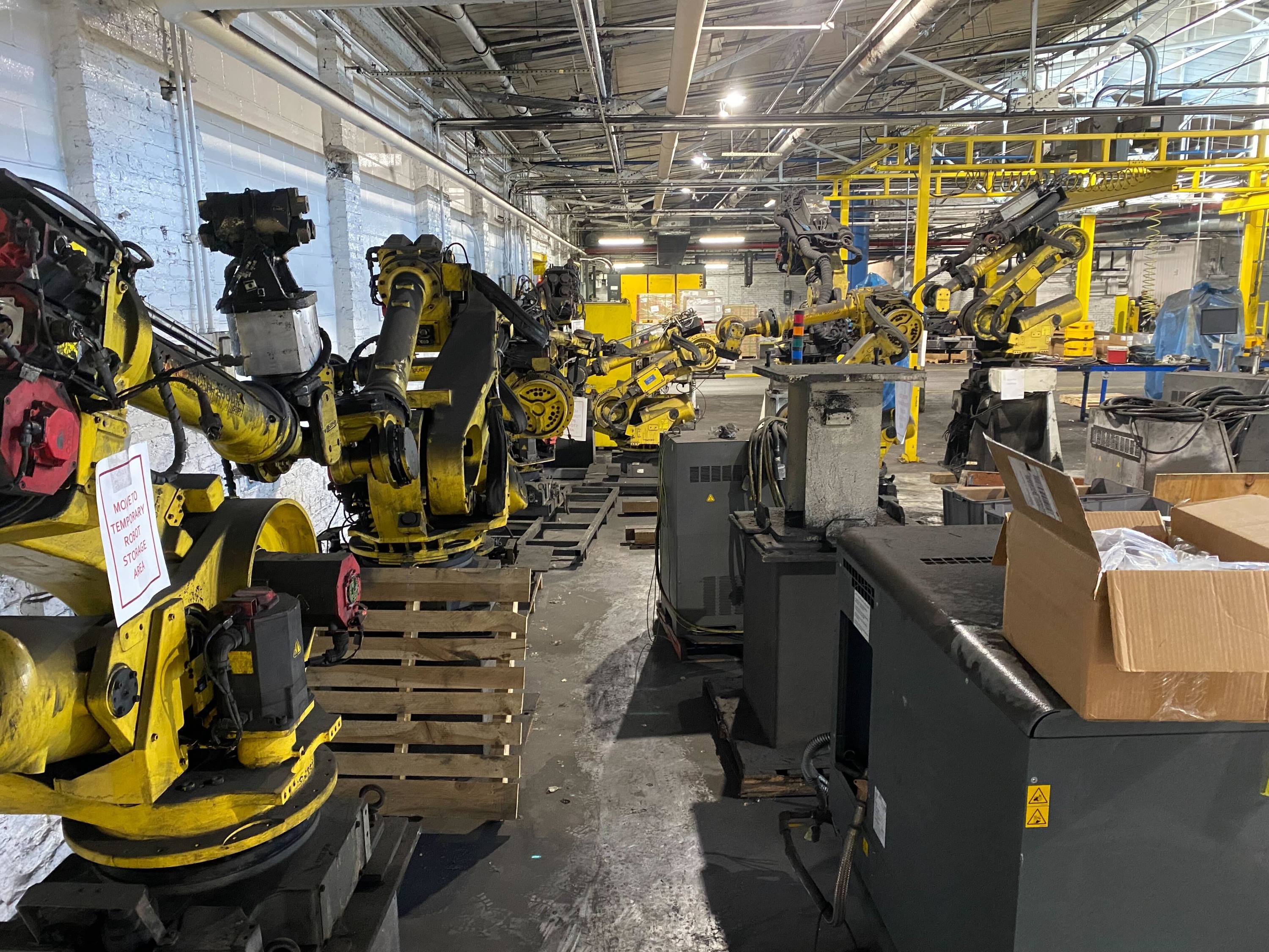 Several industrial robots sitting unused in a factory storage area.