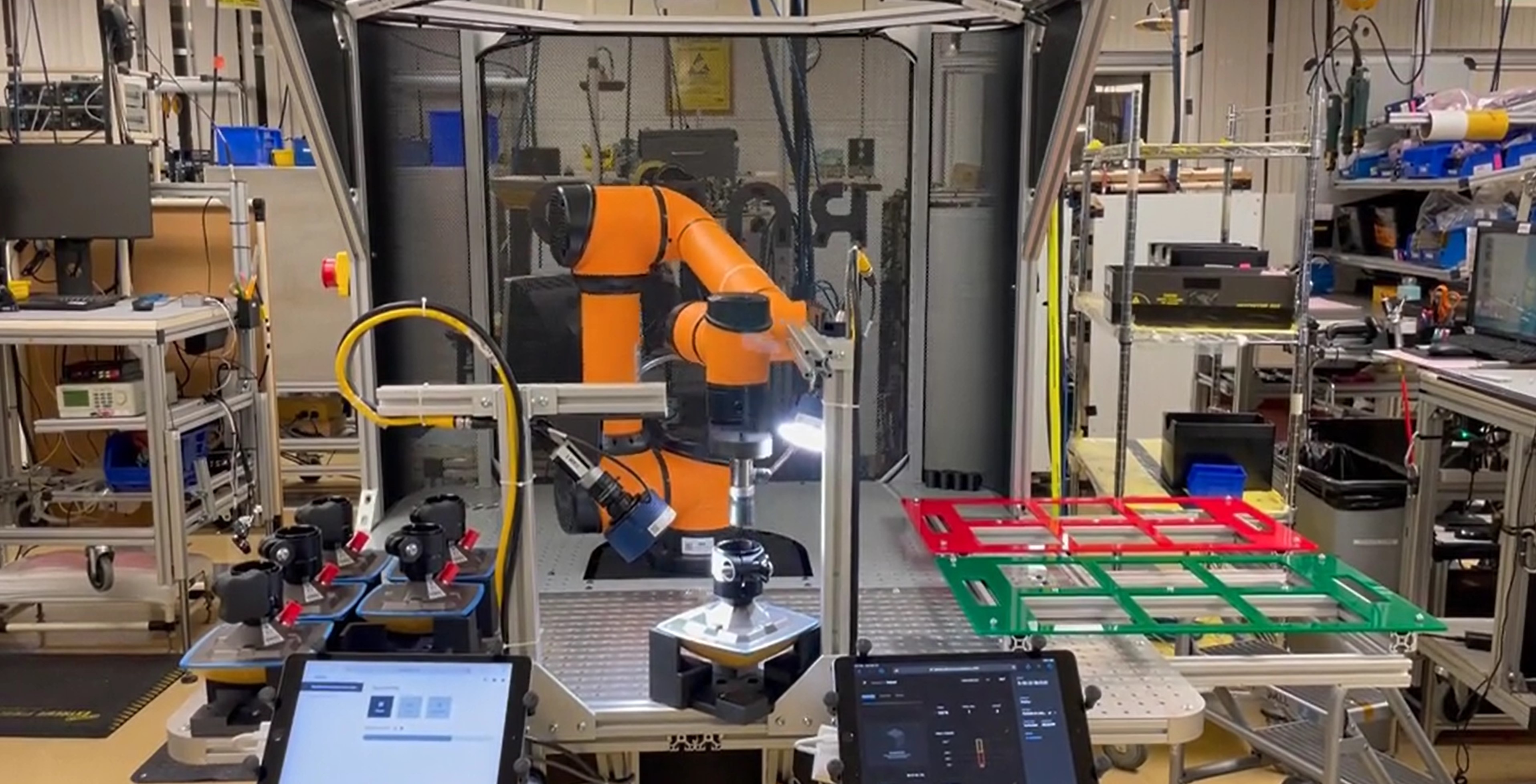 An orange Rapid Machine Operator moves Topcon GNSS antennas from an input tray to an inspection system for an Elementary camera to perform inspection. There are accept and reject trays on the right side of the work cell for sorting units after inspection.