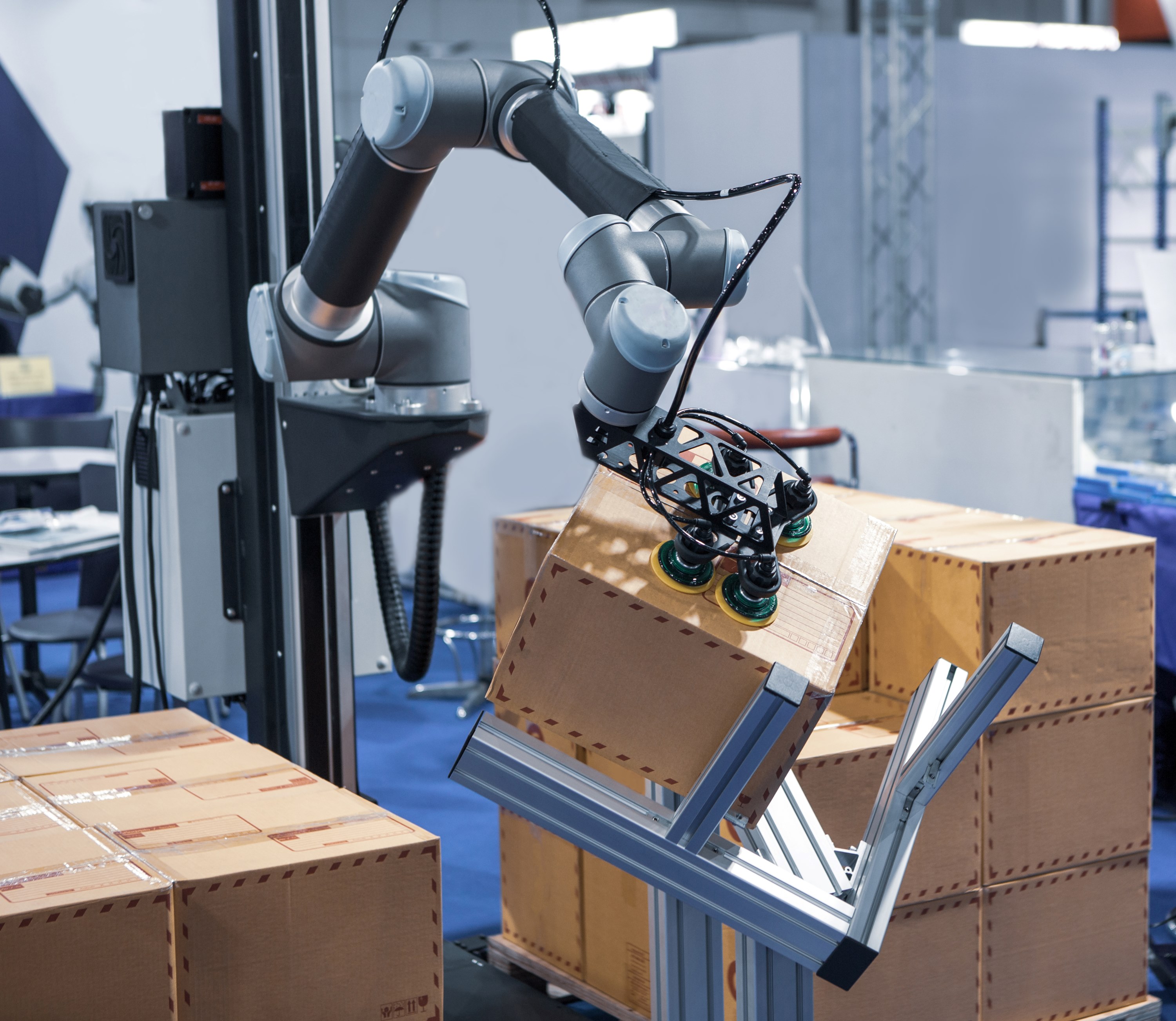 A Universal Robots cobot mounted on a vertical seventh axis picks a cardboard box from an offset fixture, to place on a pallet nearby.