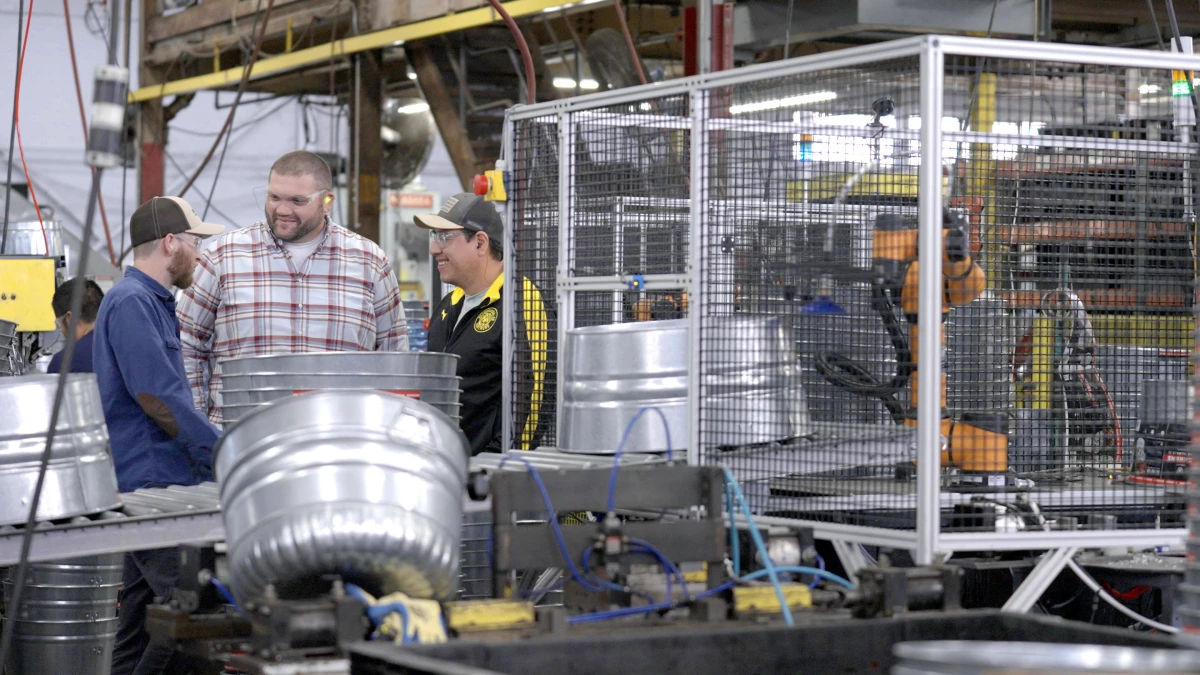 Three men smiling and talking next to a robotic workcell that is manufacturing steel wash tubs.