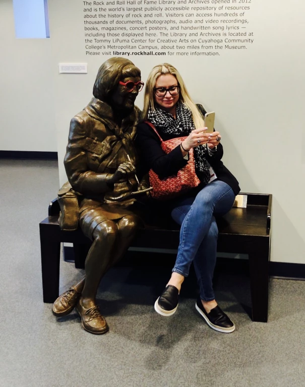 Mandy on a bench taking a selfie with a statue at the Rock and Roll Hall of Fame.