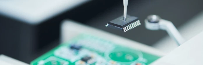 A focused shot of a microchip being carefully placed on a printed circuit board.