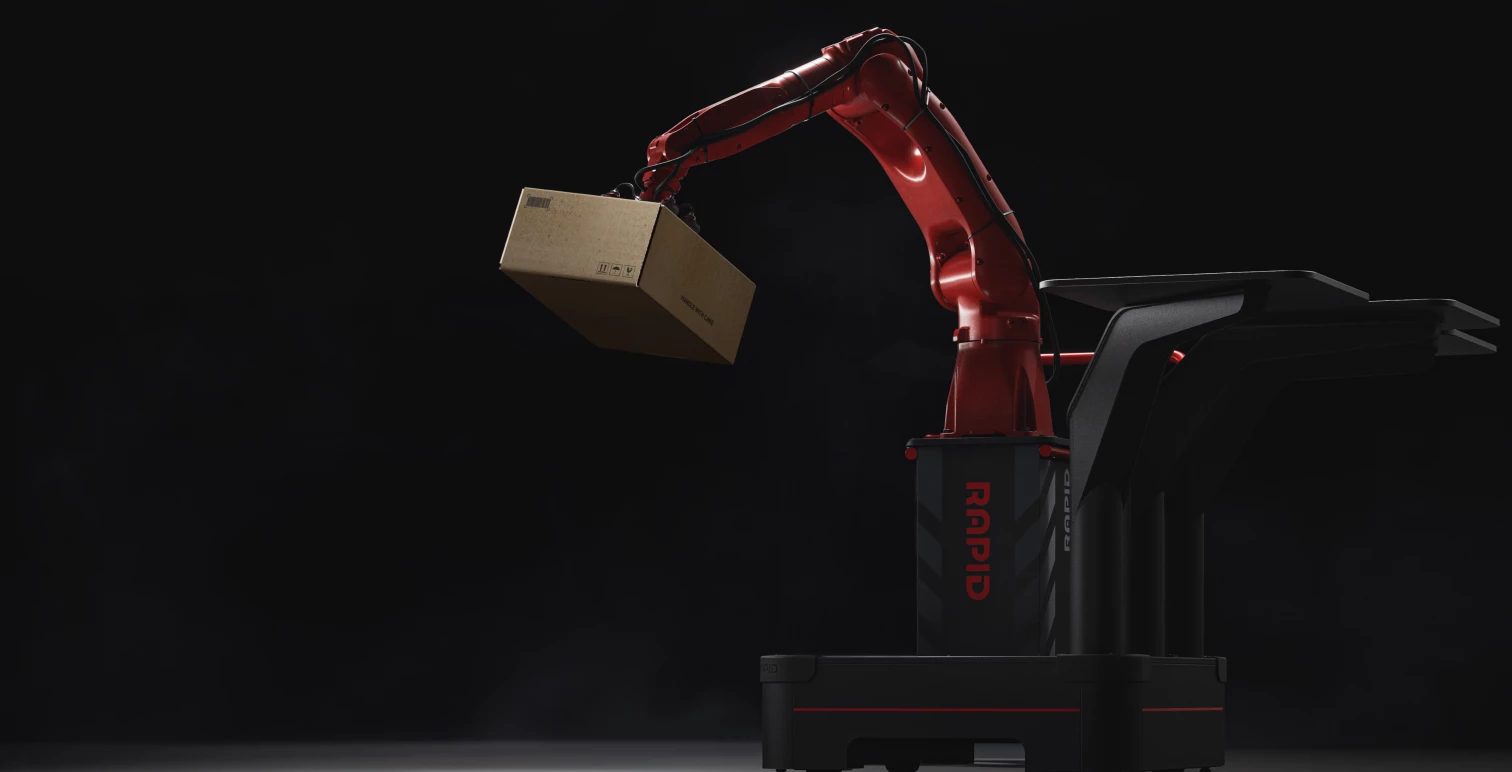 A red industrial arm on a black, modular robot base, holding a cardboard box with a suction gripper.