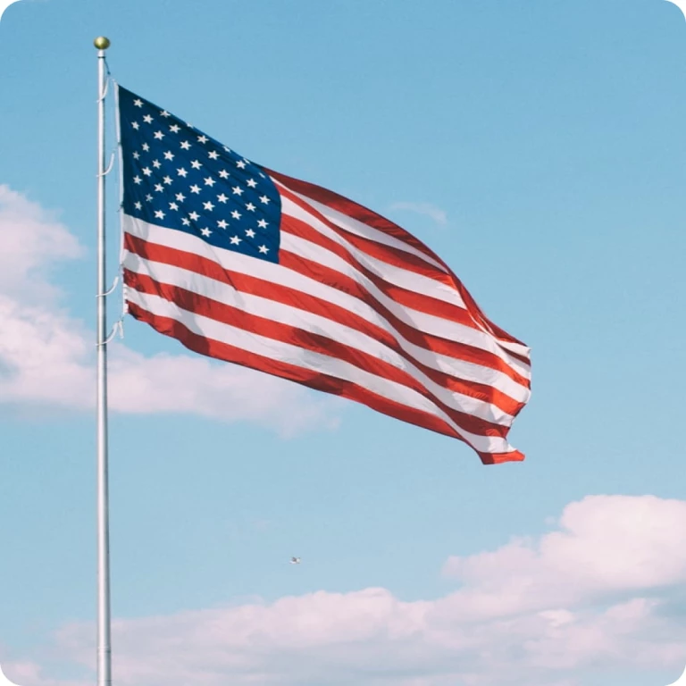 An American flag waving on the right side of a pole with cloudy skies in the background.
